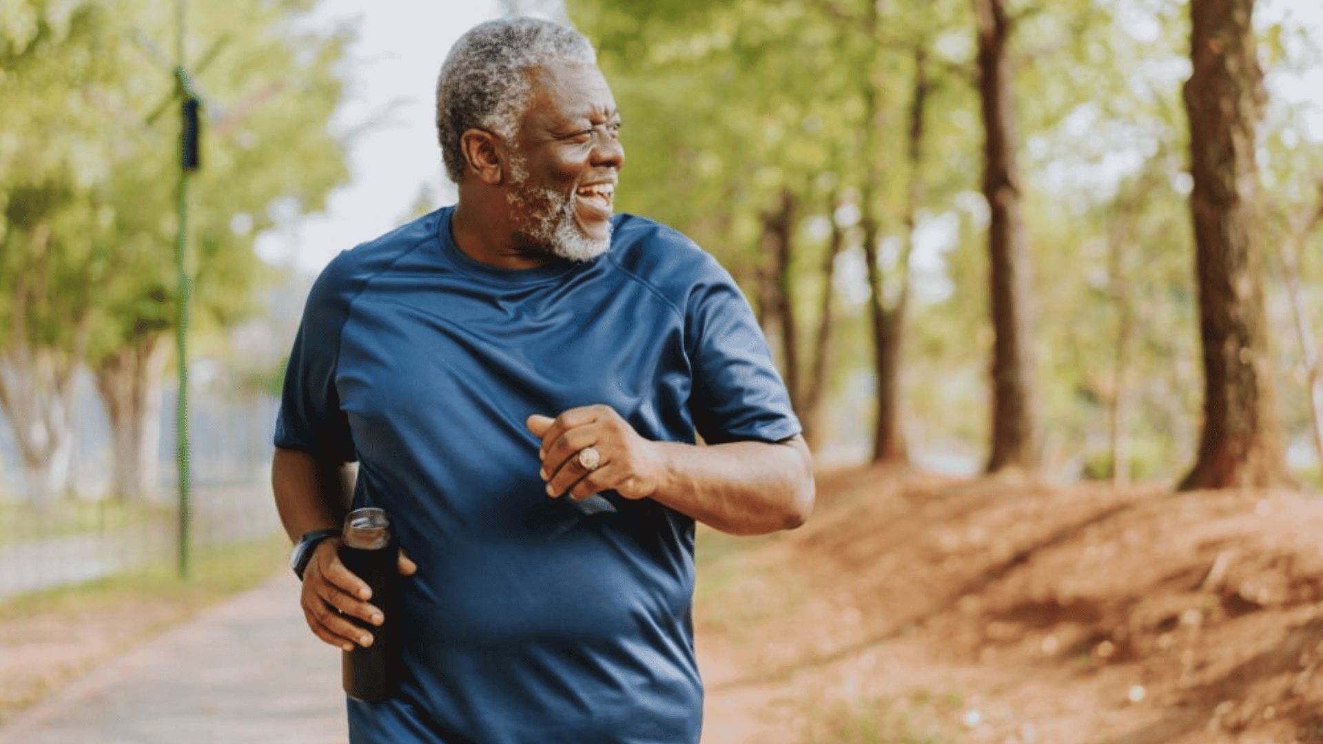 Homme senior en tenue de sport courant dans un parc, souriant et tenant une gourde, illustrant les bienfaits de l’activité physique pour la santé et la vitalité.