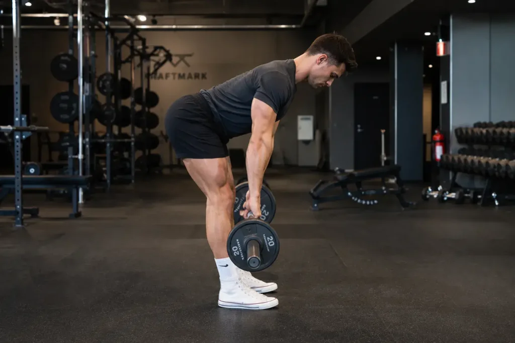 Homme en salle de sport réalisant un soulevé de terre jambe tendu avec une barre.